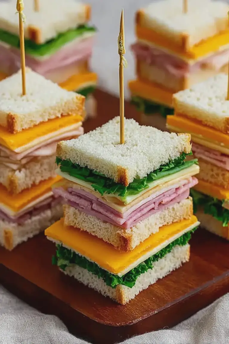 A platter of juicy mini sandwiches with cream cheese and ham, garnished with lettuce on a wooden table.