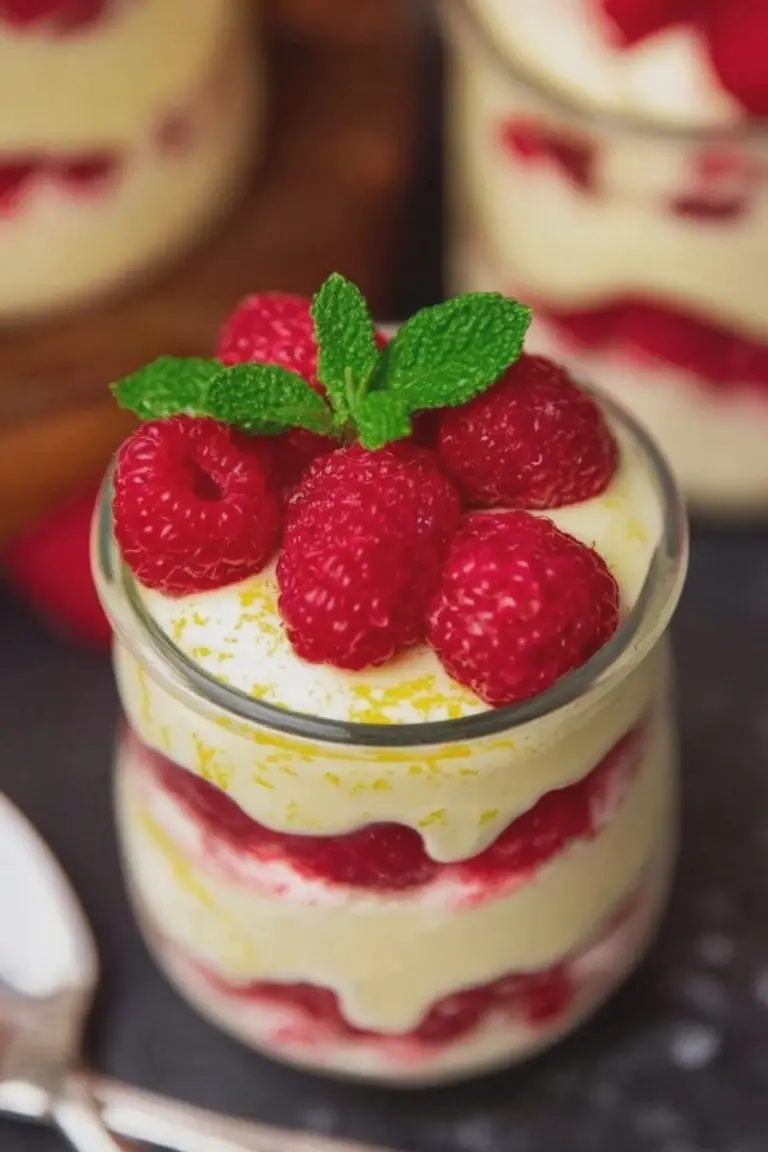 Close-up of layered Lemon Raspberry Fluff dessert in a glass jar, topped with fresh raspberries and mint leaves.