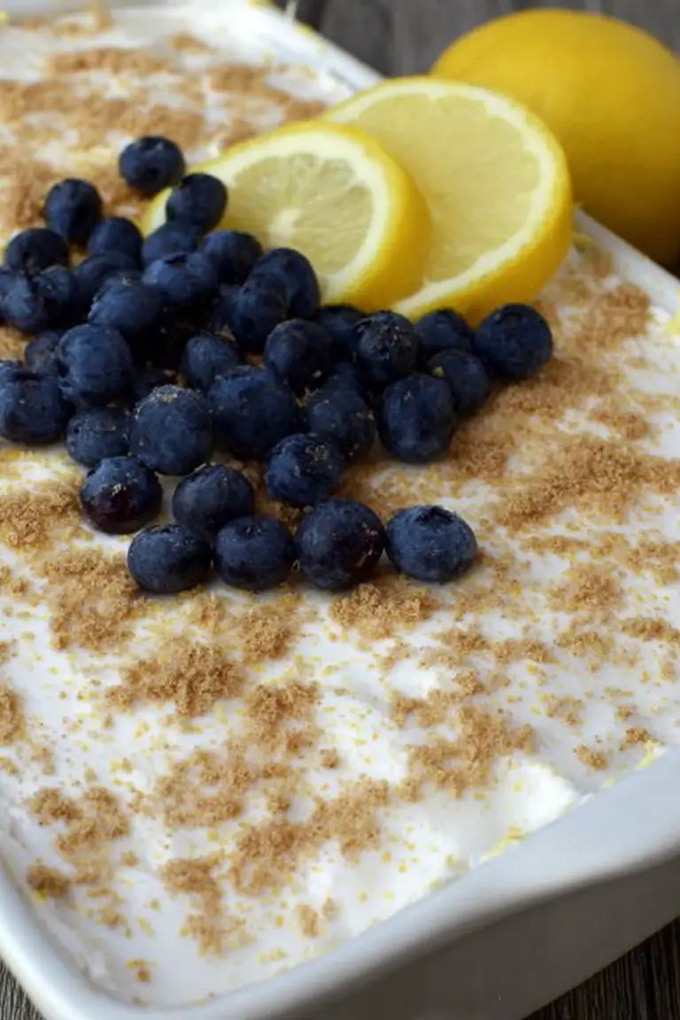 Slice of no bake lemon blueberry dessert topped with blueberries and mint on a white plate.