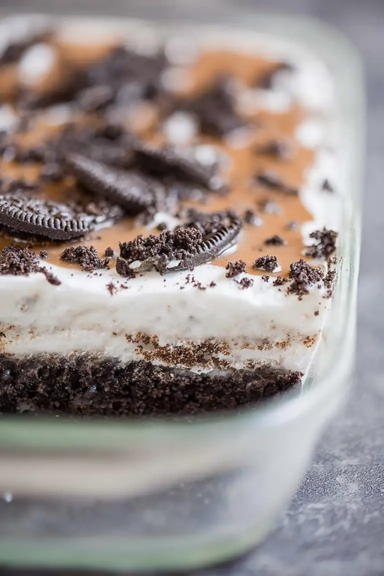 Slice of No Bake Oreo Layer Dessert with layers of cream cheese, chocolate pudding, and crushed Oreos, garnished with whipped cream on a plate.