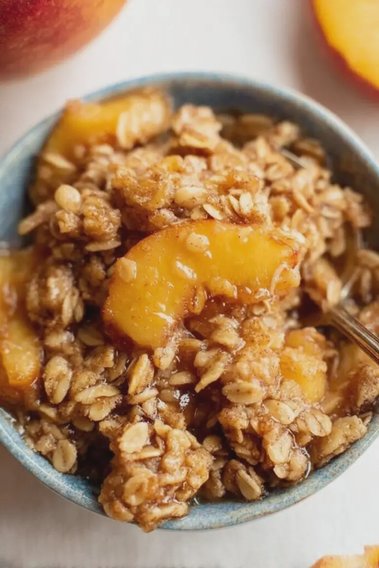 Delicious peach crisp served warm with a scoop of vanilla ice cream and mint garnish on a wooden table.