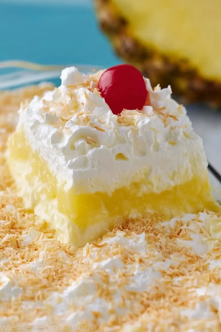 Close-up image of Pina Colada Lush dessert topped with toasted coconut and cherries, placed in a glass baking dish with tropical elements.