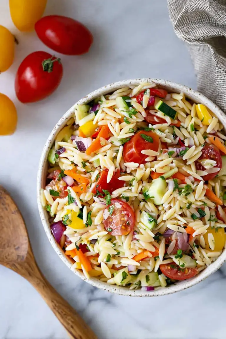 Colorful rainbow orzo salad in a bowl with cherry tomatoes, bell peppers, cucumber, red onion, feta cheese, and fresh basil.