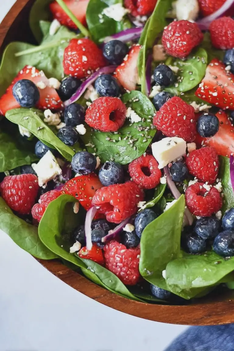 Colorful spinach berry salad with strawberries, blueberries, raspberries, feta cheese, and almonds in a bowl, served with poppy seed dressing.