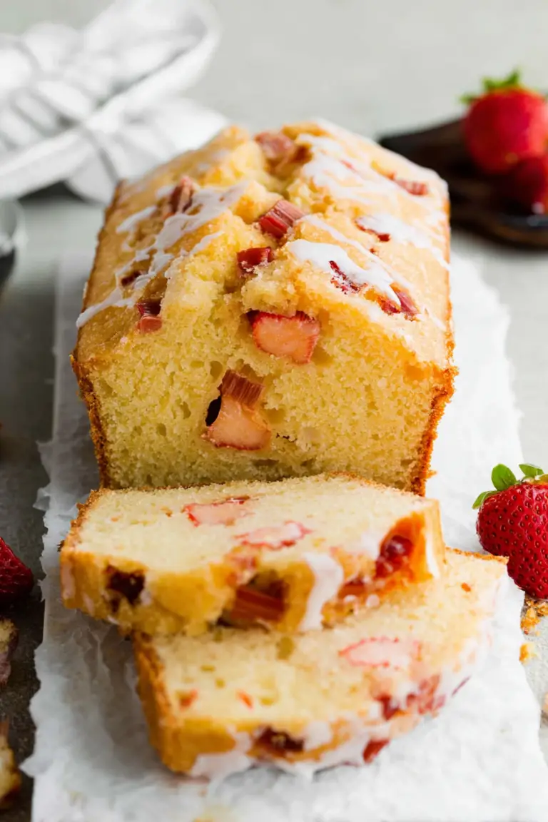 Sliced strawberry rhubarb pound cake on a rustic wooden table, garnished with fresh strawberries and rhubarb stalks.