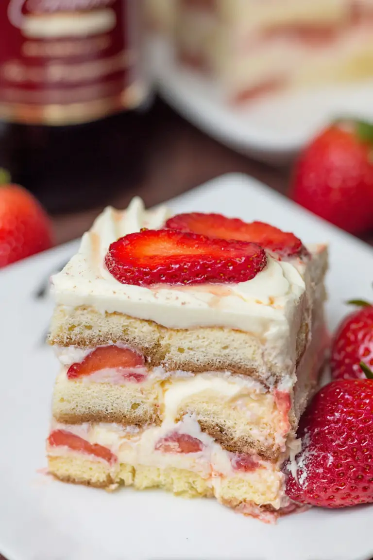 Deliciously layered strawberry tiramisu slice on a plate, garnished with fresh strawberries and mint.