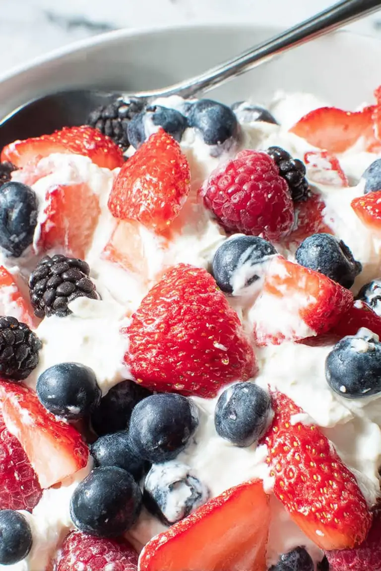 Bowl of triple berry cheesecake fruit salad featuring strawberries, blueberries, and blackberries on a rustic wooden table.