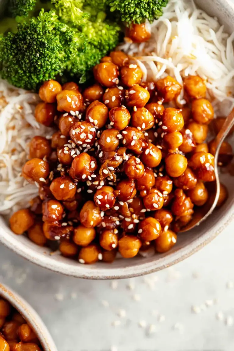 Vegan sticky sesame chickpeas served with quinoa and steamed broccoli in a bowl, topped with sesame seeds and green onions.