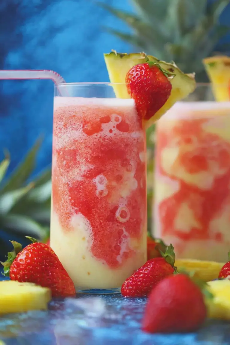 Refreshing Virgin Strawberry Pina Colada in a glass garnished with strawberry and pineapple, surrounded by tropical plants.