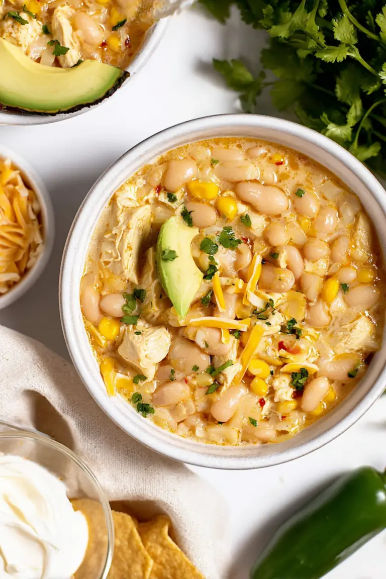 Close-up of white bean chicken chili with cilantro and sour cream in a bowl, garnished with avocado and tortilla chips.